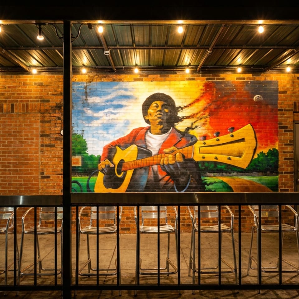 Outdoor patio with brick walls, string lights, and a vibrant mural of a person playing guitar.