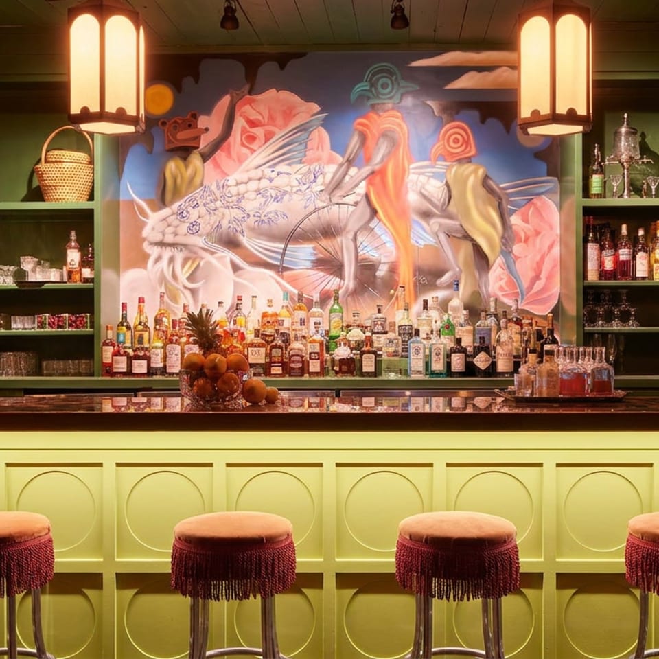 A vibrant bar with a lime green counter, orange stools, and a colorful mural behind bottles.