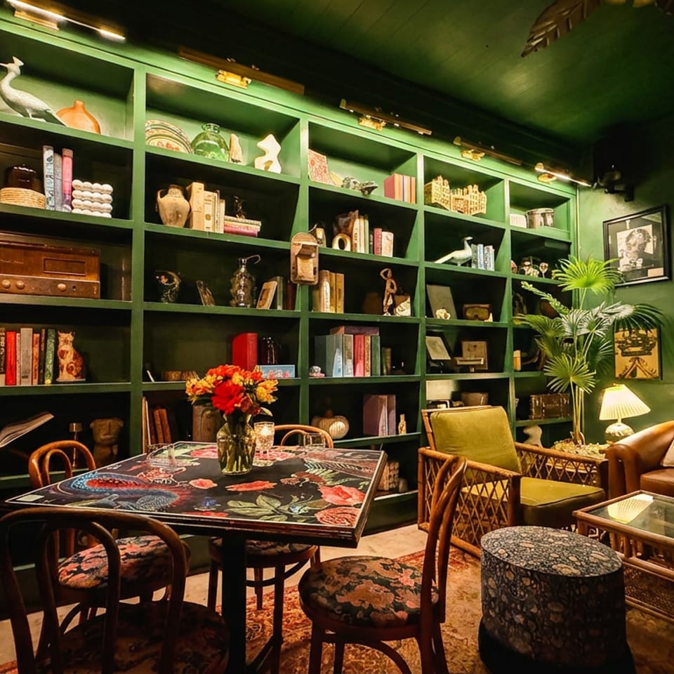 Cozy restaurant interior with dark green walls, bookshelves, a floral table, and a leather couch.